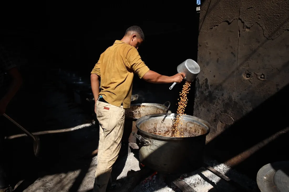 man in yellow shirt cooking food in large pot