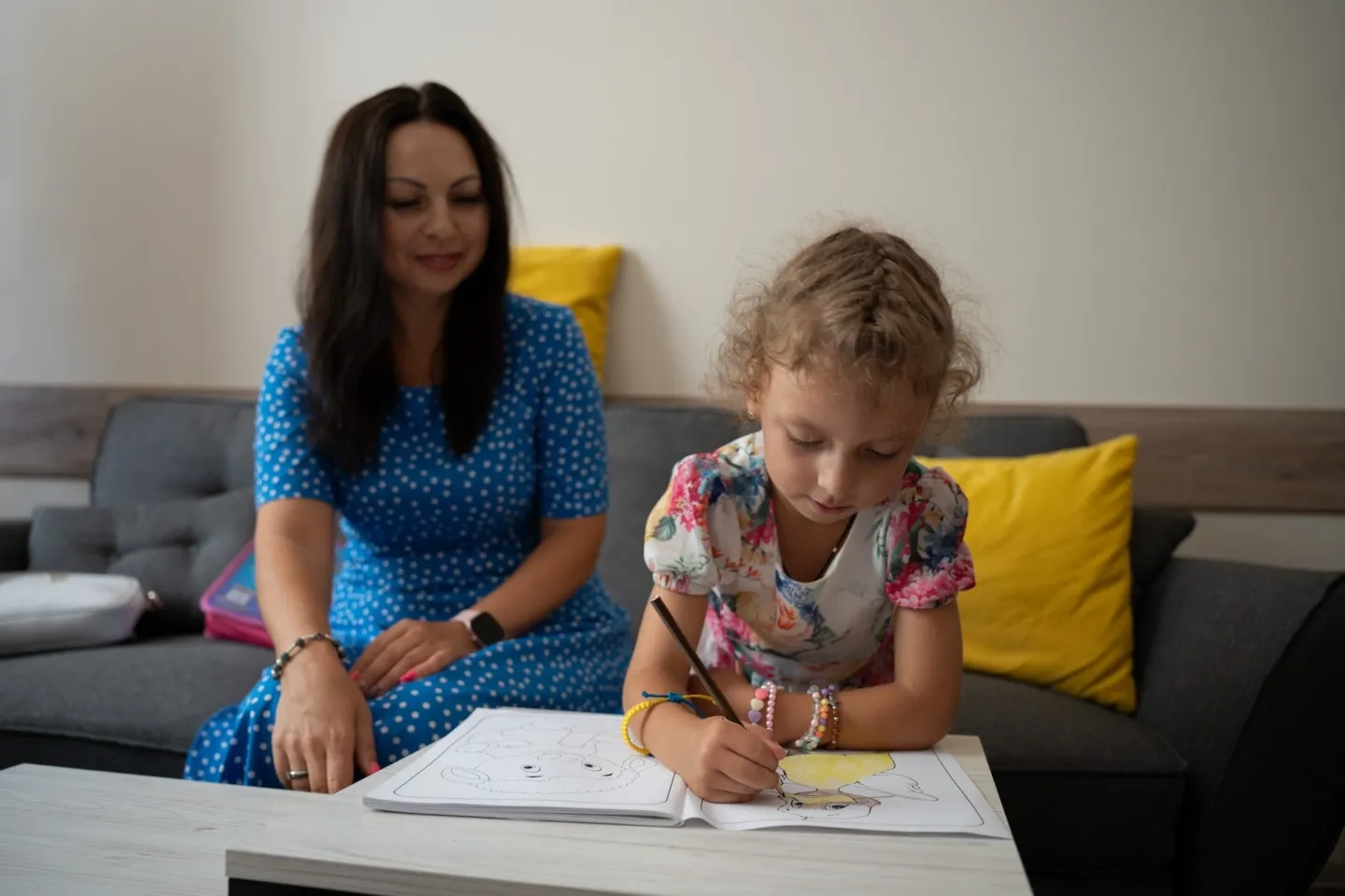 young girl colors while her mother looks on