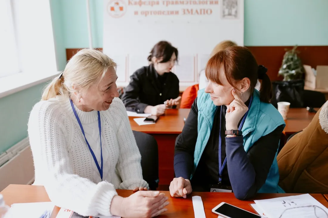 two women looking at each other and speaking at a desk
