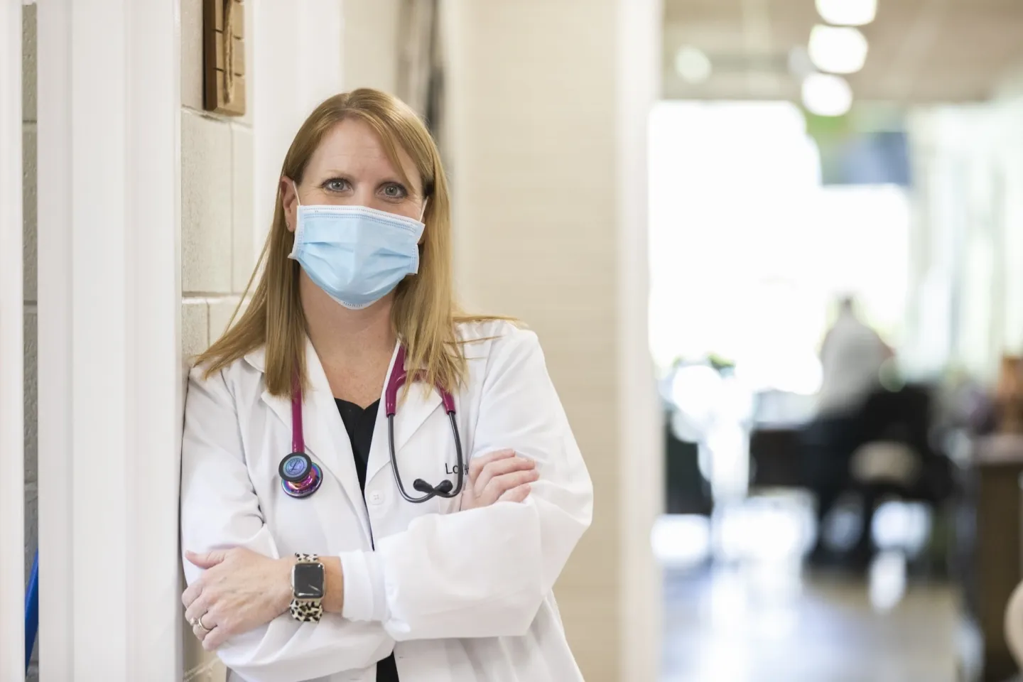 Community health worker in a white lab coat and mask poses for the camera.