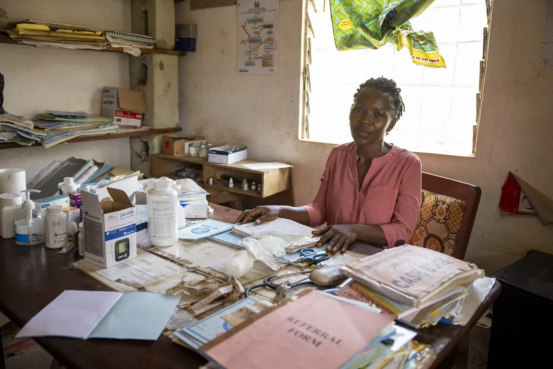 A woman sits at a desk covered in medical papers
