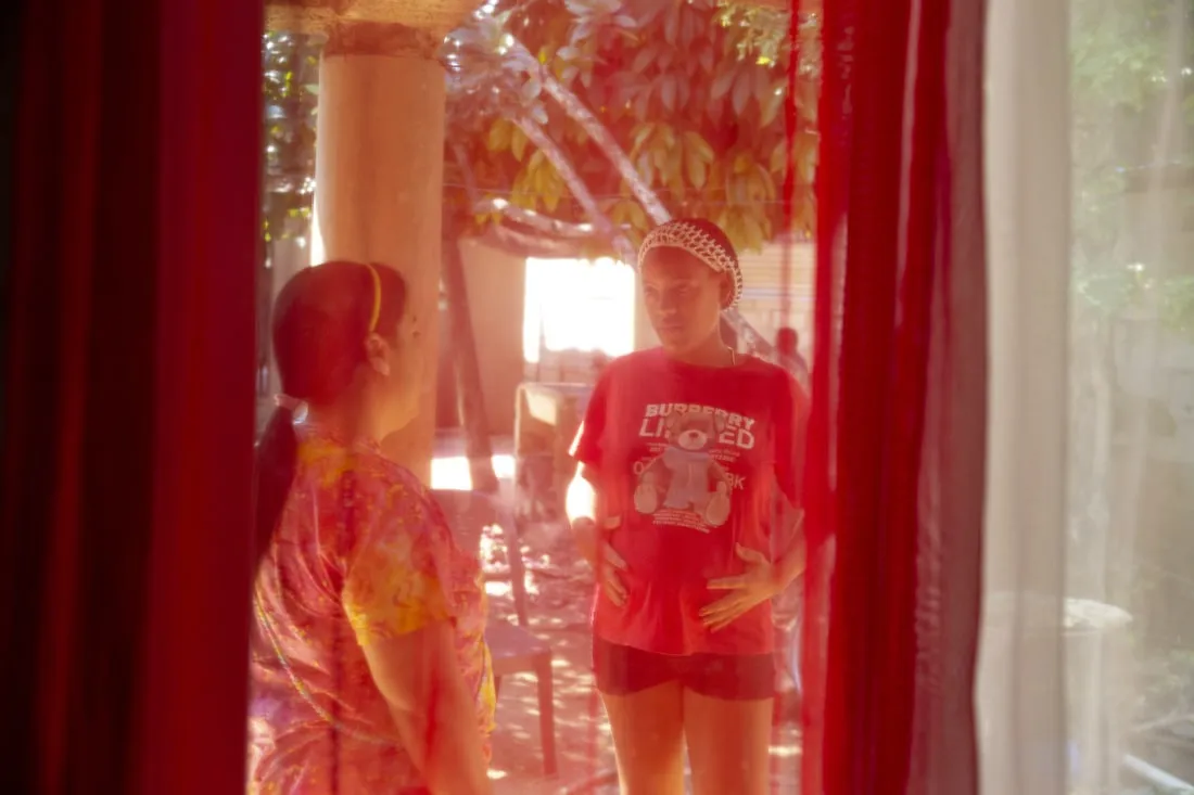 Through a red curtain giving a reddish tint, two women are standing outside talking.