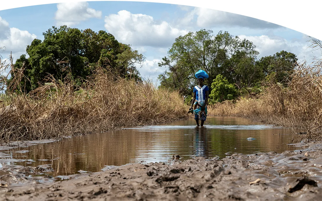 woman carrying bag on top of head through mud