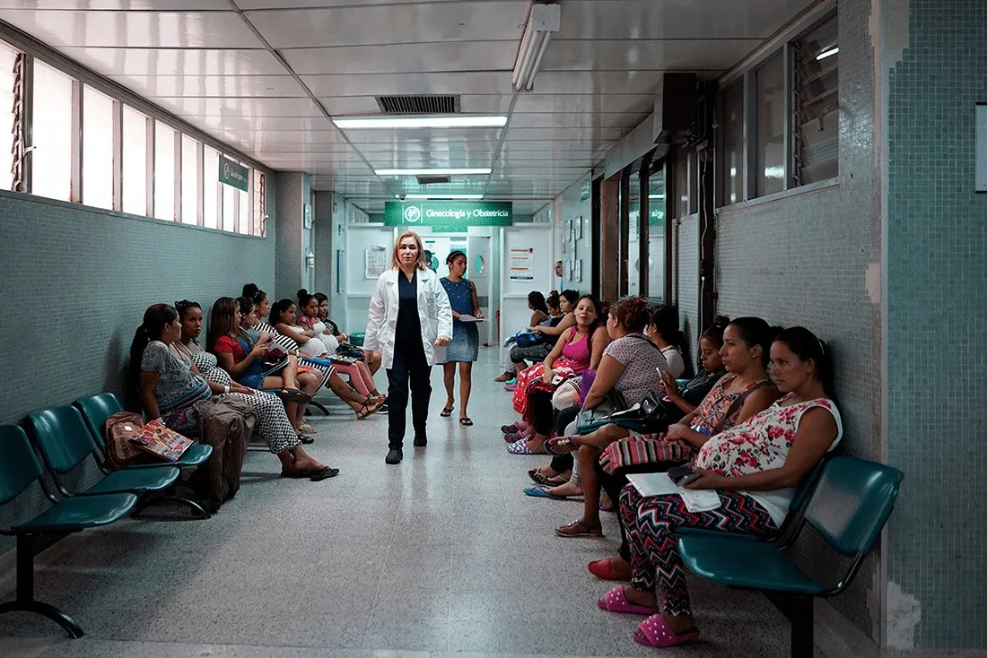 medical staff walks down hospital hallway with pregnant women sitting on both sides waiting for treatment