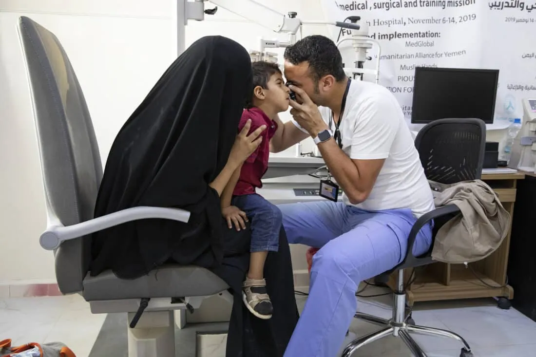 Doctor looks into eye of young boy as mother holds him