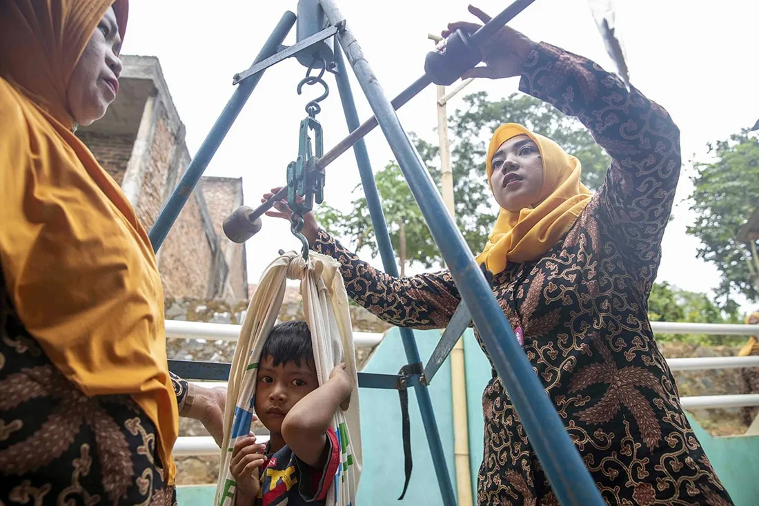 Two midwives checking on young boy's weight