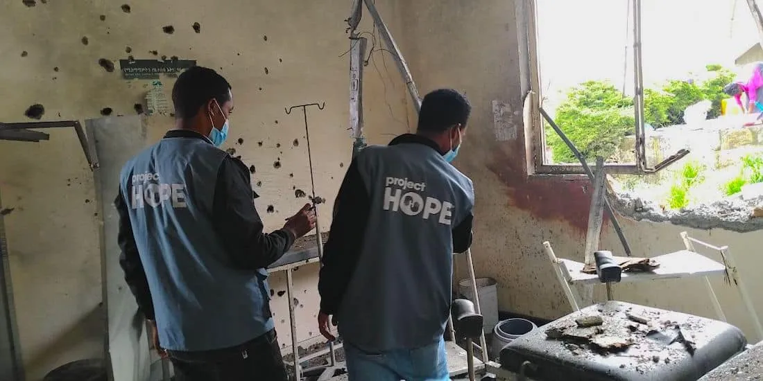 Two men in Project HOPE gear assessing damage of hospital